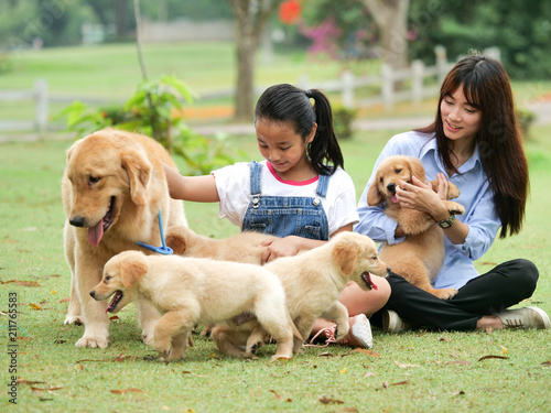 Little Asian girl and her sister playing with a cute golden retriever dog in the park.