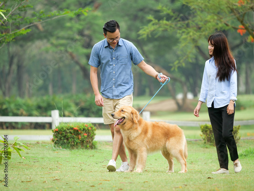 Asian couple lover walking with a cute golden retriever dog in the park together afther finish work.
