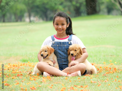 Little Asian girl playing with a cute golden retriever dog in the park.