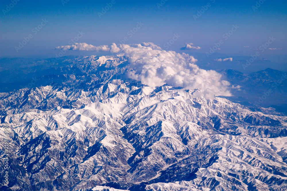 Fototapeta premium Mountains covered with snow and clouds, aerial view. Earth planet surface. Travelling around world. Environment protection and ecology. I take my earth with a little blue sky