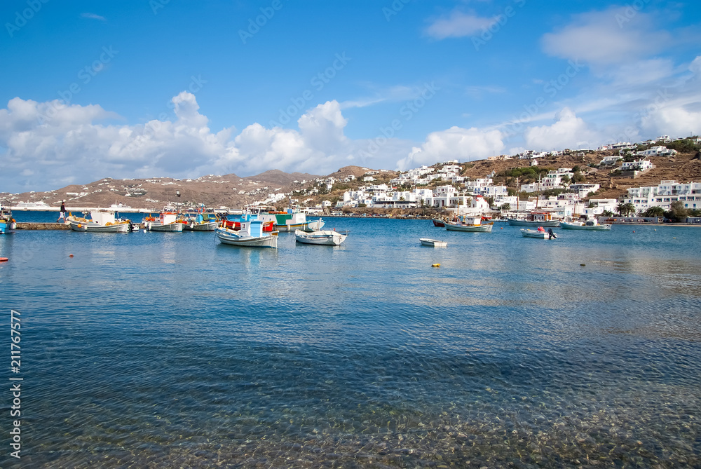 Boats on sea water in Mykonos, Greece. Sea village on cloudy blue sky. White houses on mountain landscape with nice architecture. Summer vacation on mediterranean island. Wanderlust and travelling