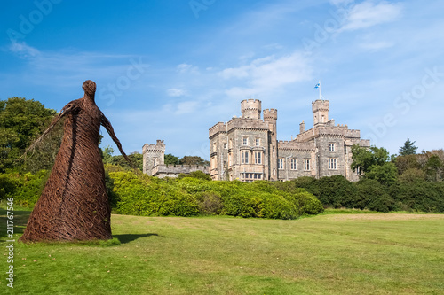 Wicker woman statue and castle in Stornoway, United Kingdom. Willow sculpture on green grounds of Lews Castle estate. Architecture and design. Landmark and attraction. Summer vacation and wanderlust photo