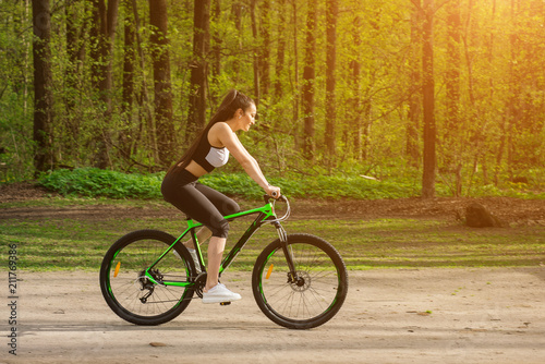 Young woman in a sport bike suit with a bicycle in the park. Health and relaxation.