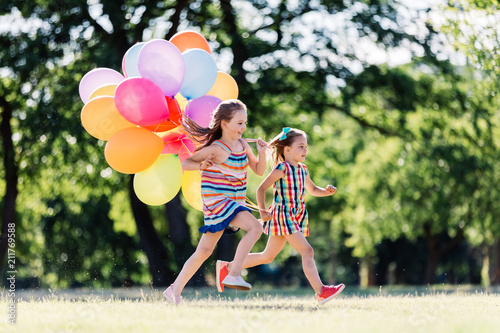 Two little happy girls running with a bunch of colorful balloons.