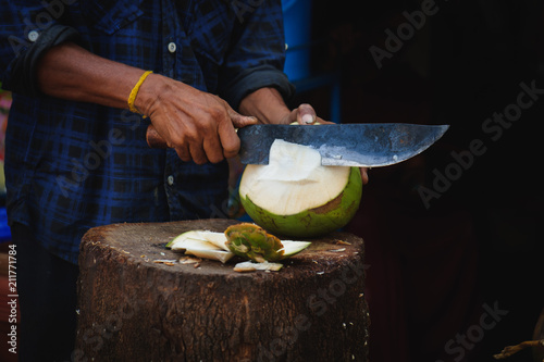 A man is cutting a fresh young green coconut with a sharp chopper or aruval for tourists photo