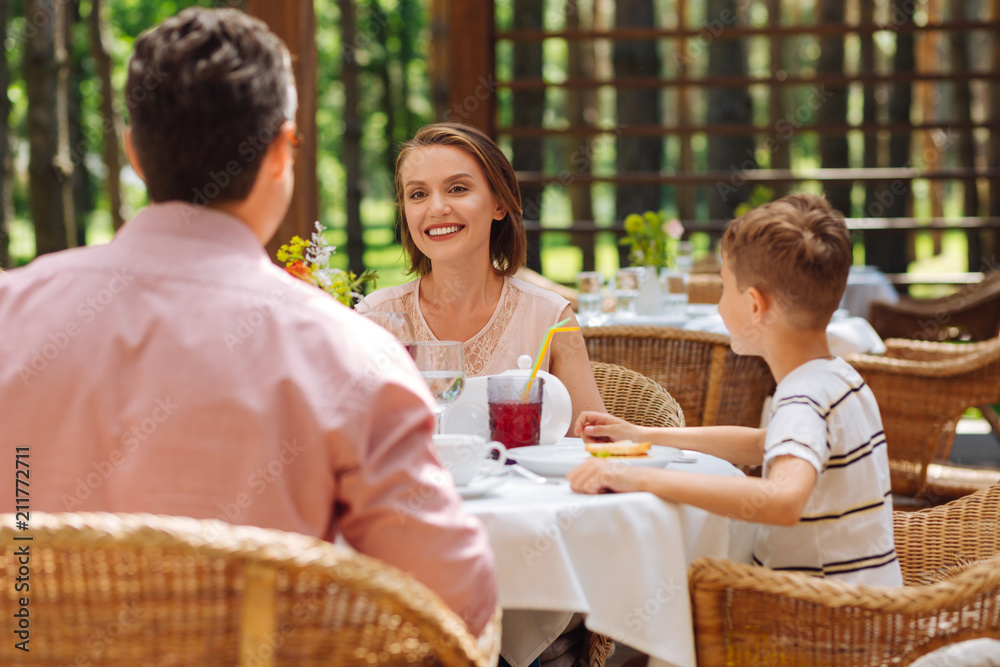 Family woman. Beaming family woman looking at her husband and son while discussing plans for the upcoming weekend Family woman. Beaming family woman looking at her husband and son while discussing plans for the upcoming weekend
