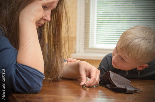 A sad woman at the table thinks the last coins. Empty wallet - boy son calms mother.