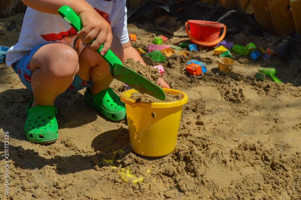 the child is playing in the sandbox. around are scattered various toys and tools for construction the child is playing in the sandbox. around are scattered various toys and tools for construction