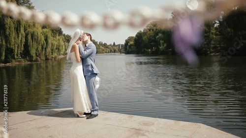 Close-up view of the love lock wrapped in the pupple ribbon at the background of the beautiful kissing couple of newlyweds near the riber bank. photo