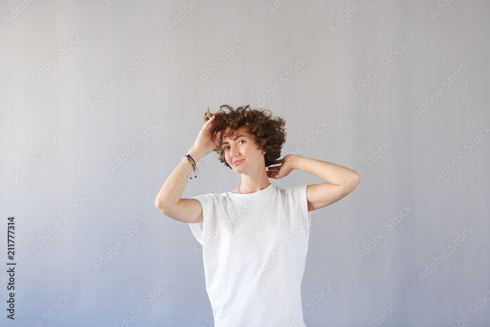 Young wonderful girl keeps herself for curly head, rejoices in her youth, has great good mood. Copy space, gray studio background. Happy joyful female student smiling Young wonderful girl keeps herself for curly head, rejoices in her youth, has great good mood. Copy space, gray studio background. Happy joyful female student smiling