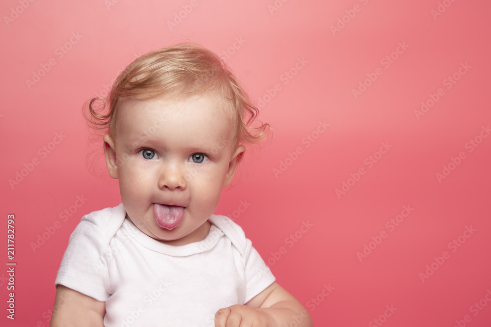 baby girl shows tongue on pink background. little girl makes an appearance baby girl shows tongue on pink background. little girl makes an appearance