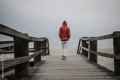 Woman in red jacket standing on the wooden pier, back view