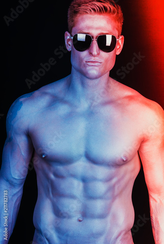 Male sunglasses & body concept. Portrait of a handsome muscular male model in trendy sunglasses posing over black background. Studio shot