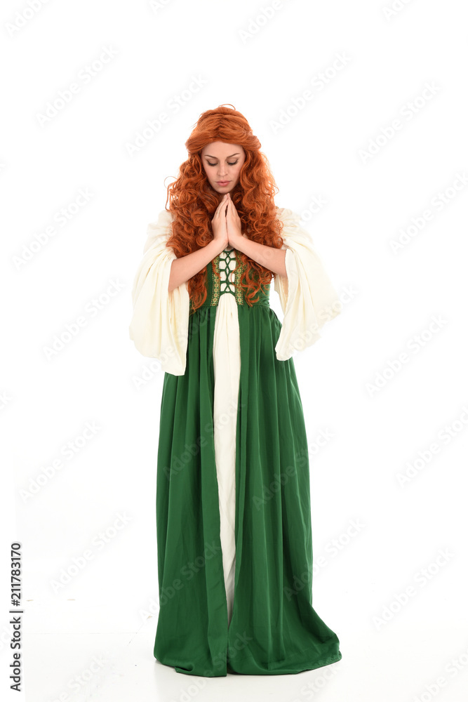 full length portrait of red haired girl wearing long green medieval gown. standing pose, isolated on white studio background. full length portrait of red haired girl wearing long green medieval gown. standing pose, isolated on white studio background.