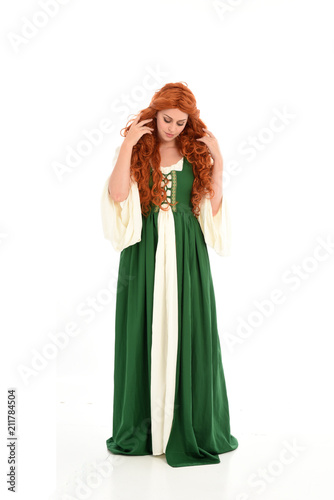 full length portrait of red haired girl wearing long green medieval gown. standing pose, isolated on white studio background.