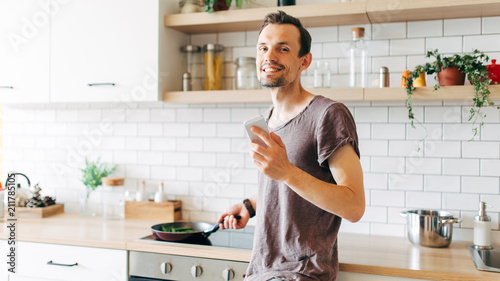 Portrait of brunet man with frying pan in his hands talking on phone in kitchen