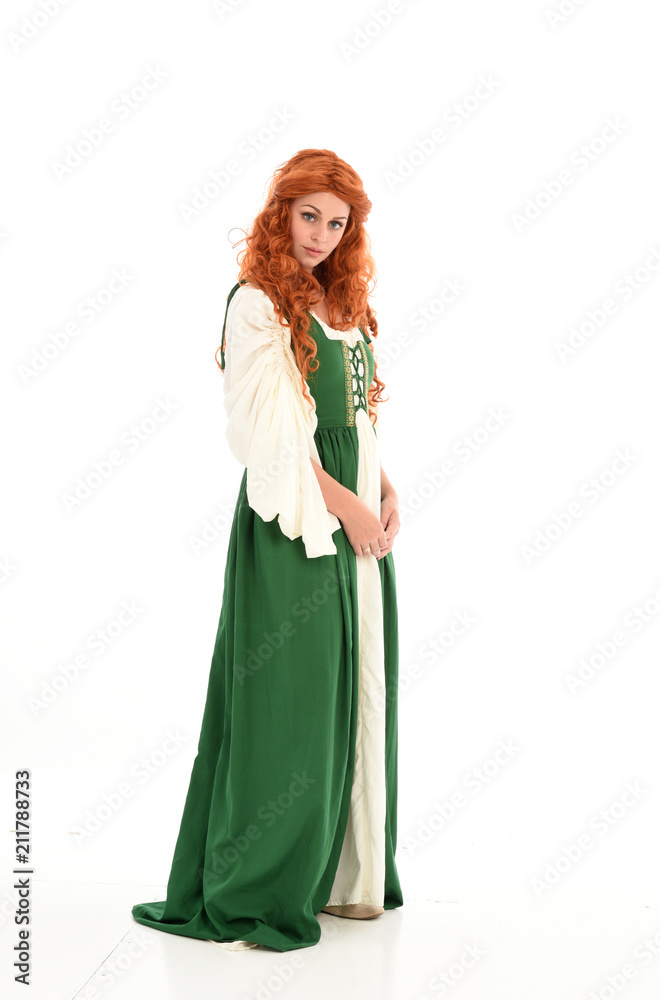 full length portrait of red haired girl wearing long green medieval gown. standing pose, isolated on white studio background.