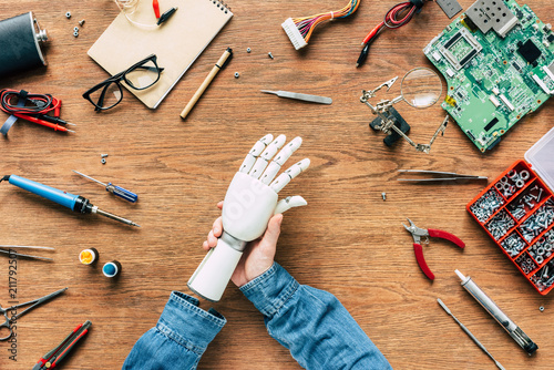 cropped image of man with amputee putting on robotic hand on table with tools