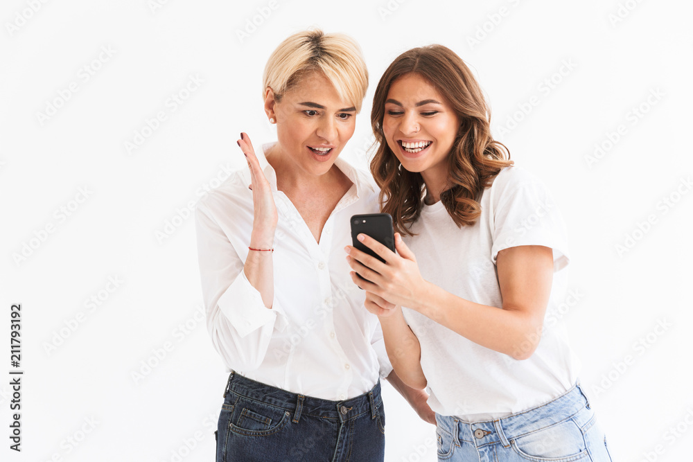 Portrait of two amazed surprised women mother and daughter holding and using black smartphone with surprise, standing isolated over white background Portrait of two amazed surprised women mother and daughter holding and using black smartphone with surprise, standing isolated over white background