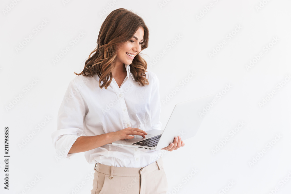 Portrait of adorable smiling woman with long brown hair holding and looking at silver laptop, isolated over white background in studio Portrait of adorable smiling woman with long brown hair holding and looking at silver laptop, isolated over white background in studio