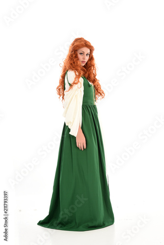 full length portrait of red haired girl wearing long green medieval gown. standing pose, isolated on white studio background.