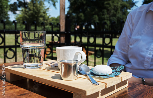 Young woman in a garden restaurant with a glass of water, coffee and milk photo