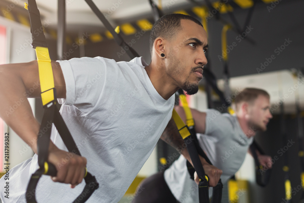 Men performing TRX training in gym Men performing TRX training in gym