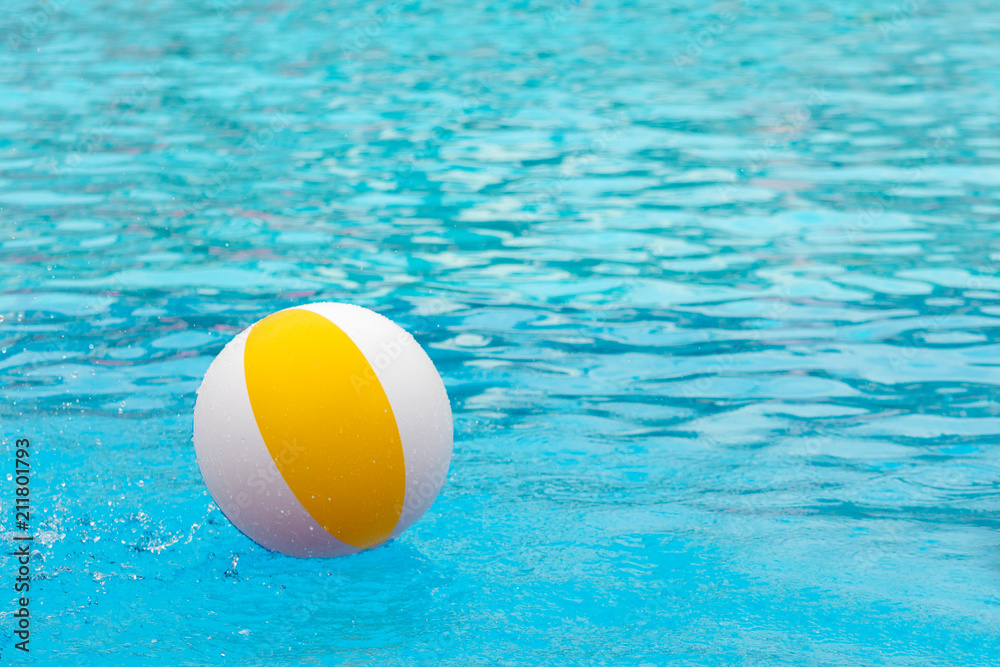 Beach ball floating in a blue swimming pool. Summer background.