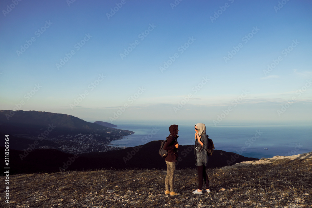 Two girls traveler stand on the top of the mountain, look down, jump, rejoice and dance.