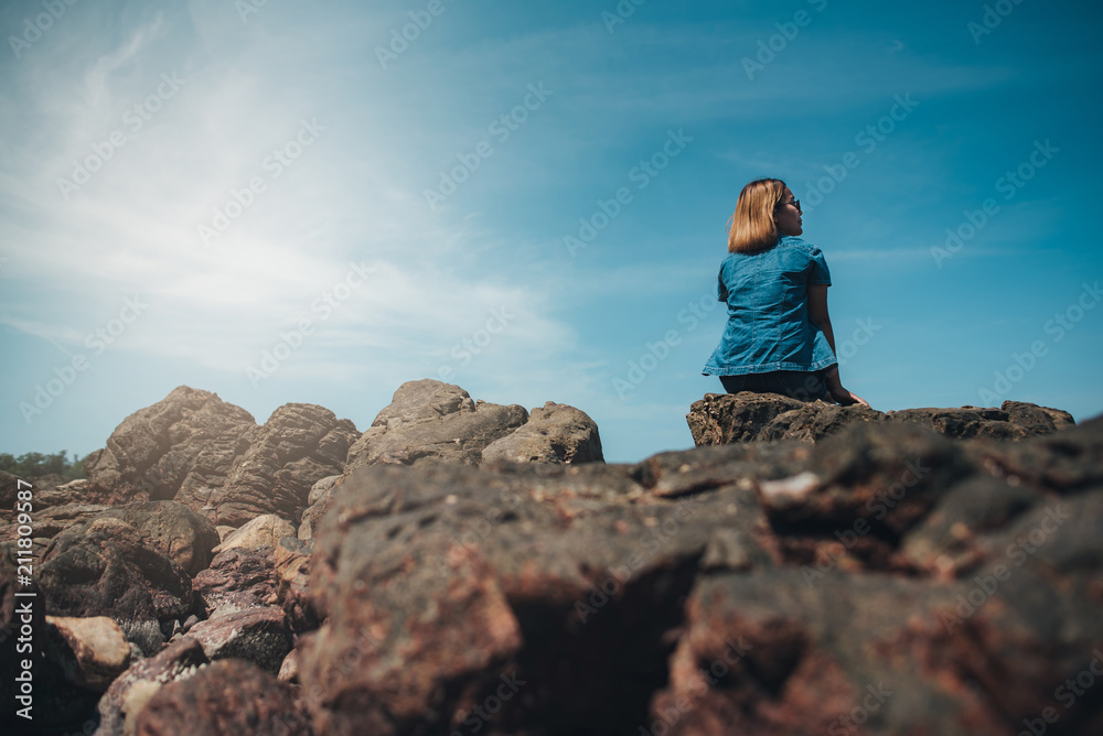 Woman sitting on a rock Beautiful girl looks at the beautiful sky by the sea. Woman sitting on a rock Beautiful girl looks at the beautiful sky by the sea.