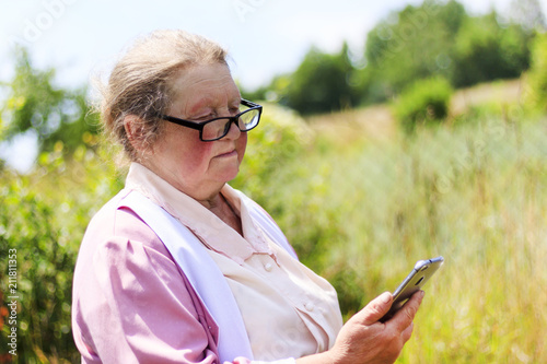 Elderly woman in the street wearing glasses looks at the mobile phone photo