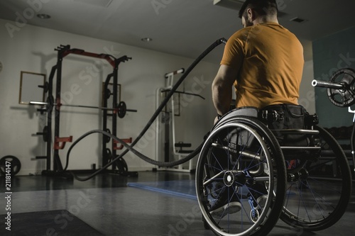 Rear view of handicapped man exercising with battle ropes in gym