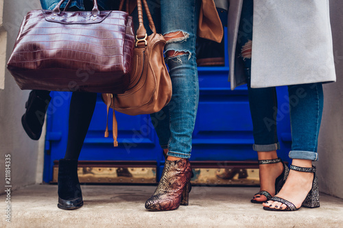 Three women wearing stylish shoes and accessories outdoors. Beauty fashion concept. Ladies holding female handbags
