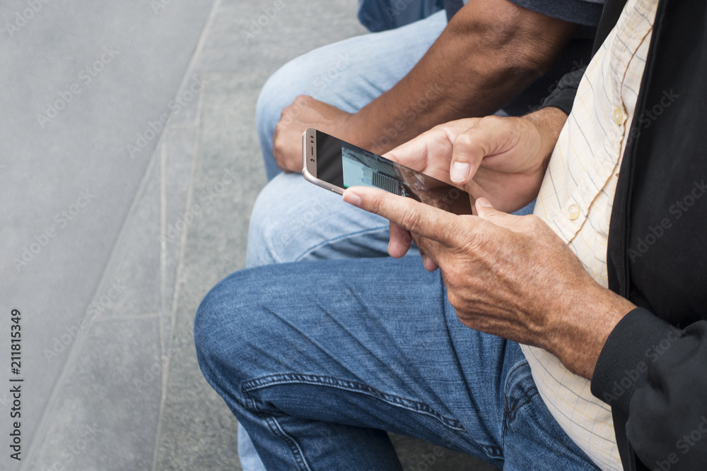 older man sitting on a bench holding and looking at his cell phone with people sitting next to him older man sitting on a bench holding and looking at his cell phone with people sitting next to him