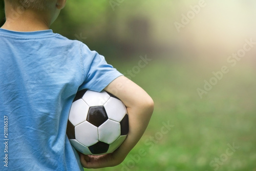 football in the hands of a boy in a blue t-shirt on a green background of nature © Dudzenich