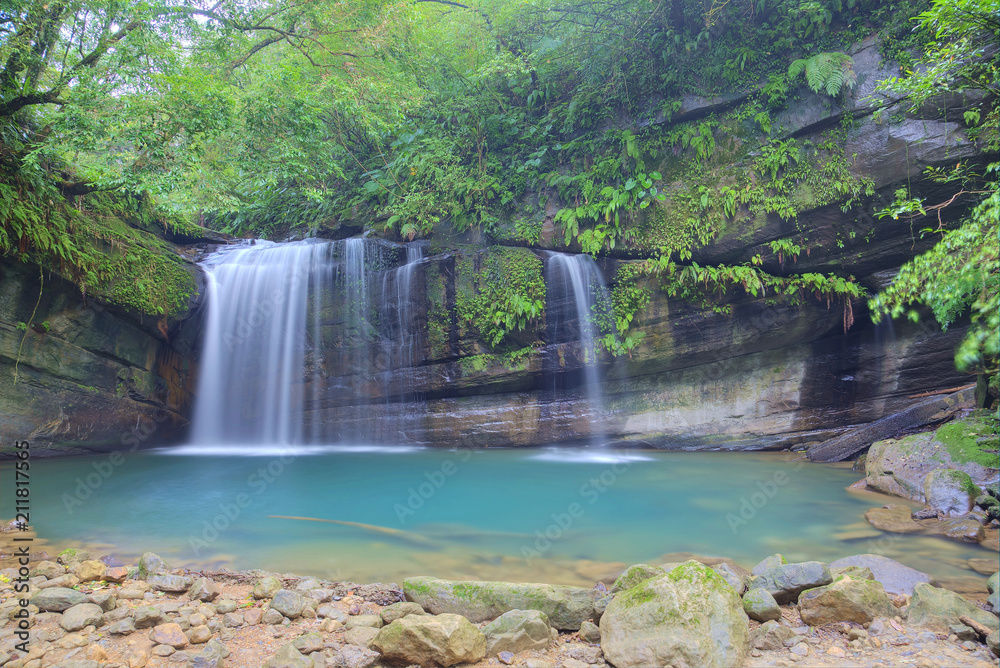 Fototapeta premium A cool refreshing waterfall tumbling down the cliff into an emerald pond hidden in a mysterious forest of lush greenery ~ Scenic view of a beautiful waterfall and intriguing river potholes in Taiwan