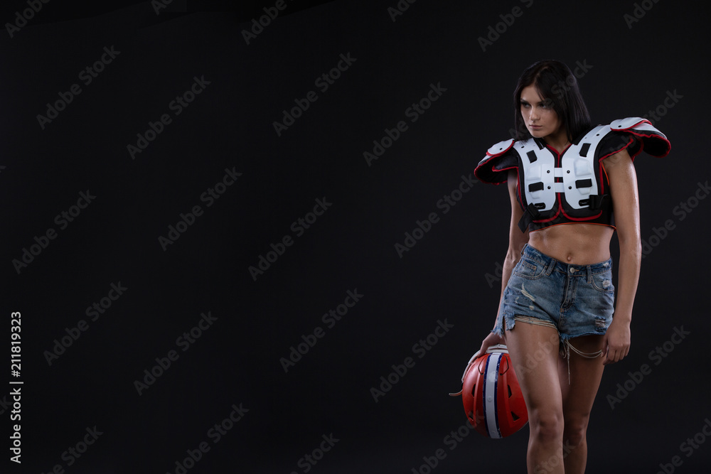incredibly beautiful, athletic brunette girl in a shoulderpads and an American football helmet demonstrating stunning amazing abs. Black background. Footy. Sexy. Having fun. Rugby
