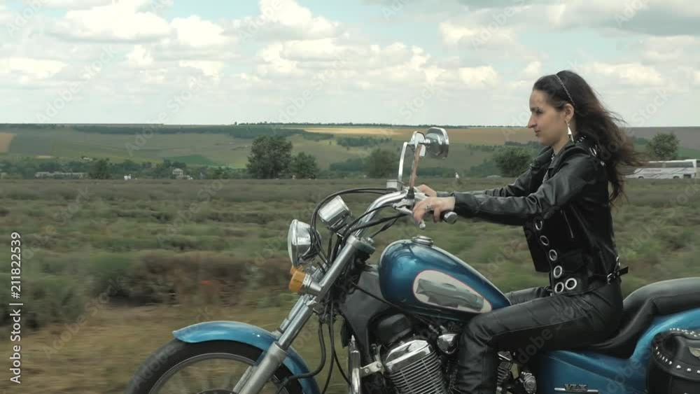 brunette biker on a motorcycle in black leather jacket. lavender field against the sky with clouds brunette biker on a motorcycle in black leather jacket. lavender field against the sky with clouds