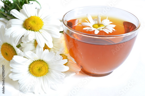 bouquet of field chamomile and glass transparent cup of brown warm tea