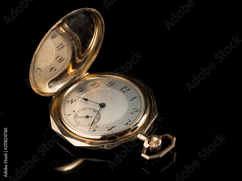 Old golden pocket watch on a black reflective surface