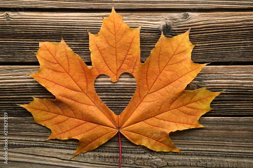 Dry maple leaf with heart on brown wooden table
