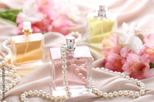 Perfume bottles with flowers and beads on satin background