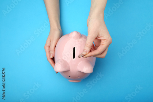 Female hand putting coin into piggy bank on blue background photo