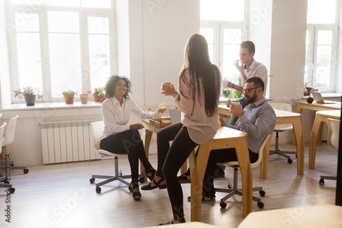 Happy multiracial workers having fun enjoying pizza together, employees spending lunch break in office talking and laughing, diverse smiling colleagues having ordered takeout meal in office chatting