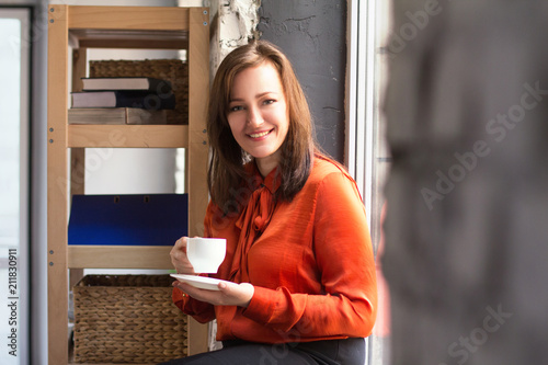 Female office assistant smiling while having cup of coffee. Happy young beautiful businesswoman holding coffee cup and looking at camera with genuine smile on her face.