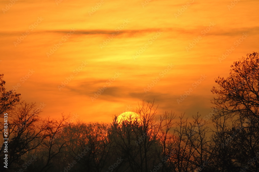 A flaming winter sunrise fills the sky with color. A light covering of clouds allows the entire disc of the sun to be visible to the naked eye creating an inspiring spectacle.