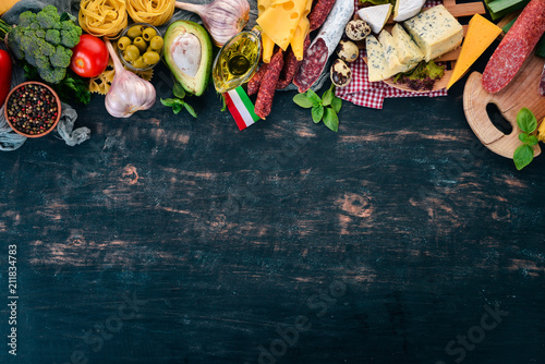 Assortment of sausage, cheese and fresh vegetables. Italian cuisine. On a black wooden background. Top view. Copy space.