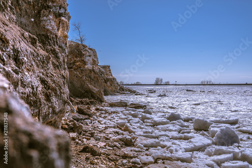 Winter Rock Cliff with trees on top and rocky ice beach