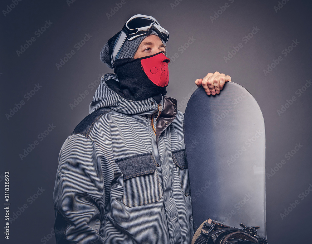 Portrait of a snowboarder dressed in a full protective gear for extream snowboarding posing with snowboard at a studio. Isolated on the gray background. Portrait of a snowboarder dressed in a full protective gear for extream snowboarding posing with snowboard at a studio. Isolated on the gray background.