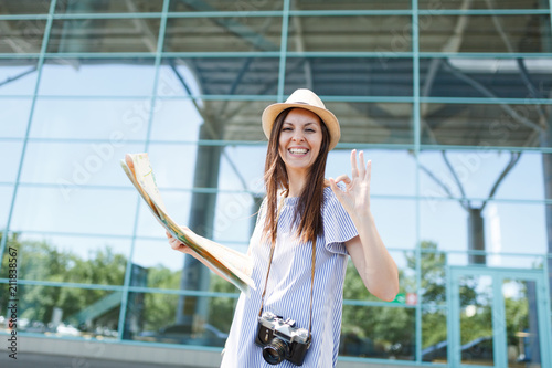 Young joyful traveler tourist woman with retro vintage photo camera hold paper map  show OK gesture at international airport. Female passenger traveling abroad on weekends getaway. Air flight concept.